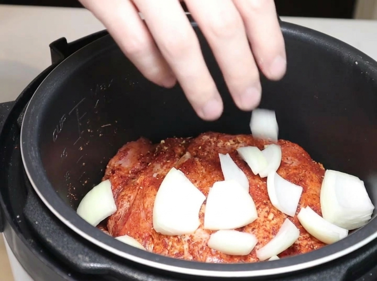 Zwiebelspalten und getrocknete Chilischoten werden zum Fleisch in den Kocher gegeben.