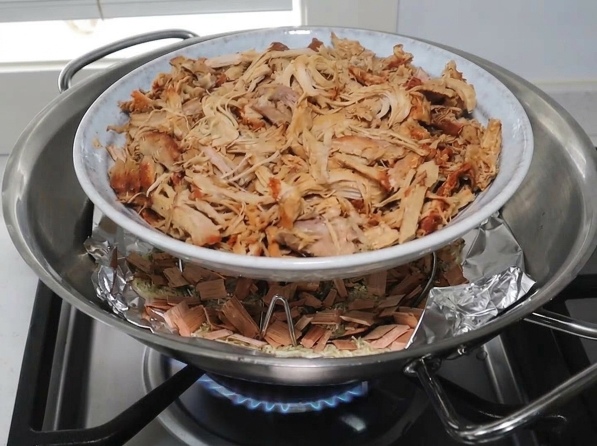 Gezupftes Schweinefleisch liegt auf einem Rost über der Räuchermischung im Wok.