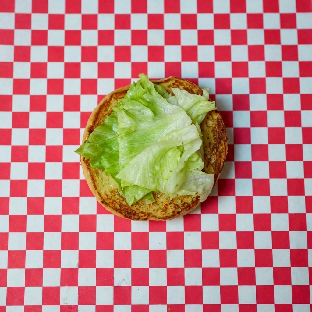 Frischer Salat und eine leuchtende Tomatenscheibe auf der unteren, gerösteten Brötchenhälfte.