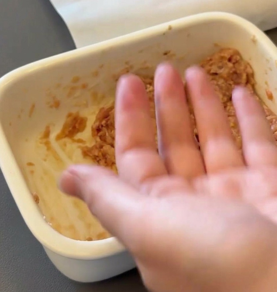 Eine Hand formt rohe Rindfleischmischung zu einem runden Patty.