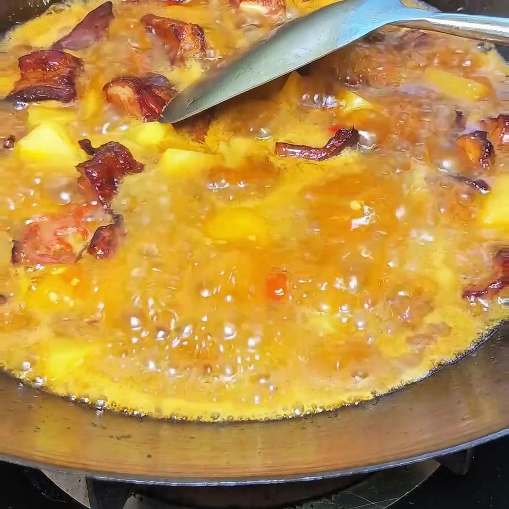 Ein Löffel cremiges weißes Schweineschmalz wird in den sprudelnden Eintopf aus Rippchen und Kartoffeln in einem Wok gemischt.