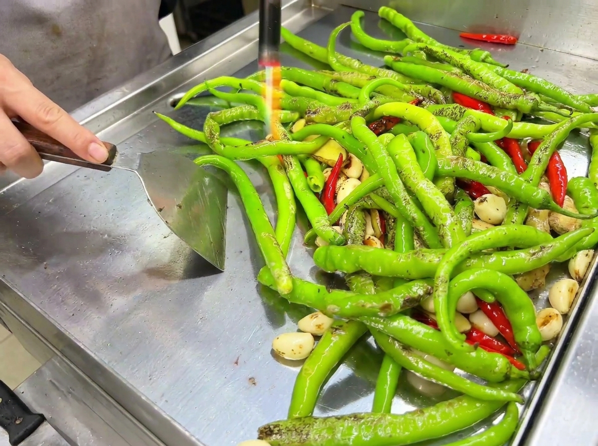 Die Flamme eines Gasbrenners röstet die Schale der Chilis auf dem Grill.