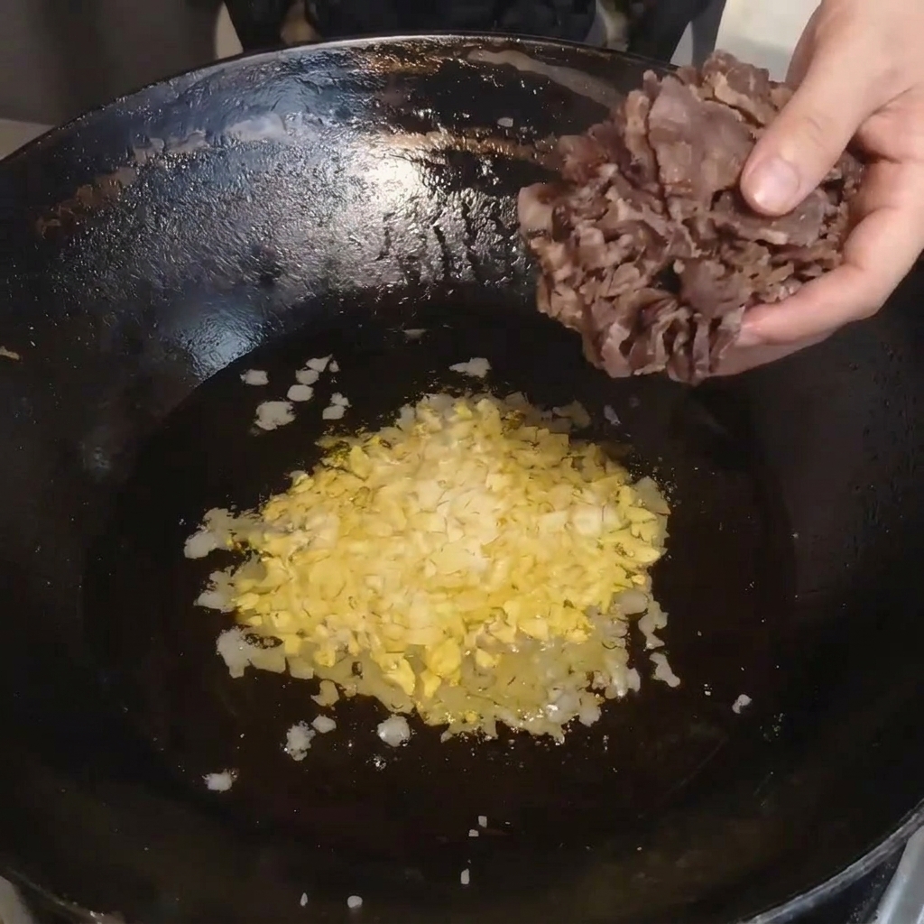Gedämpfte Pökelfleischscheiben werden aus einer Schüssel in einen heißen Wok gegeben.