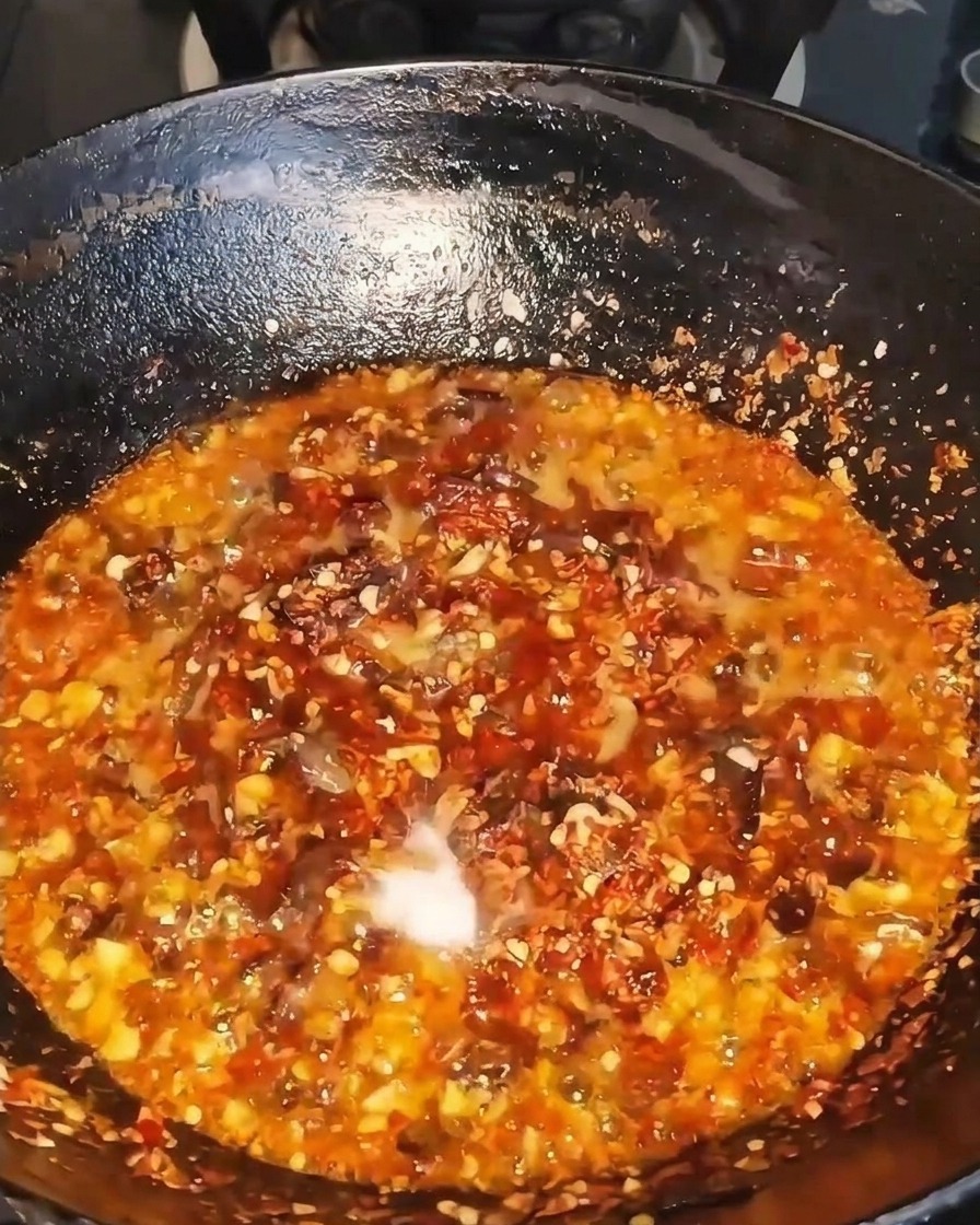 Dunkle flüssige Würze wird in einen brutzelnden Wok voller Rindfleisch, Chili und Aromaten gegossen.