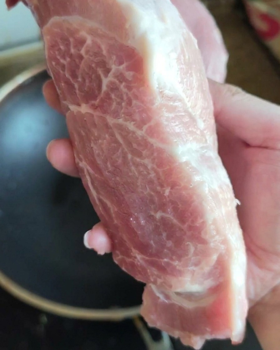 Ein großes, frisches Stück rohe Schweineschulter wird in die Kamera gehalten.