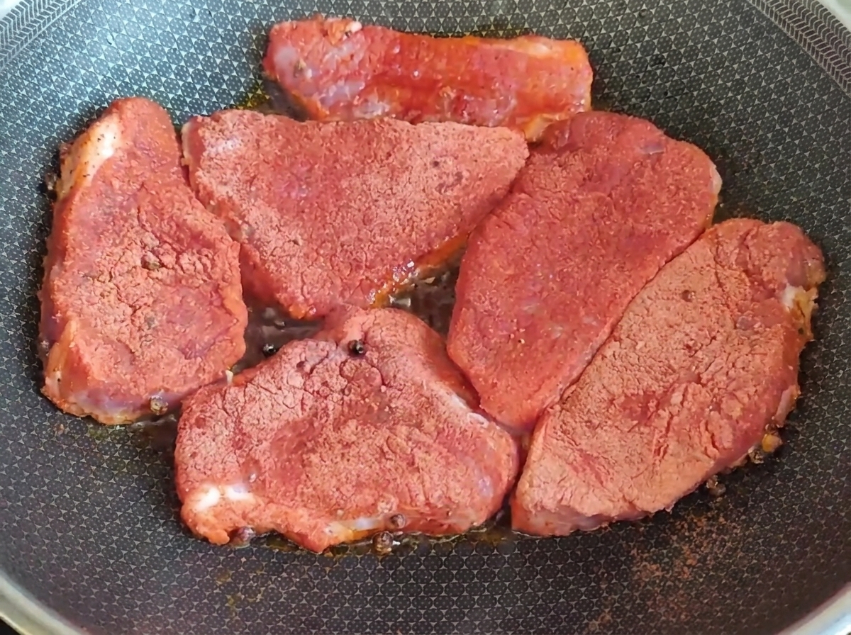 Mit Gewürzen eingeriebene rohe Fleischstücke braten in einer heißen Pfanne.