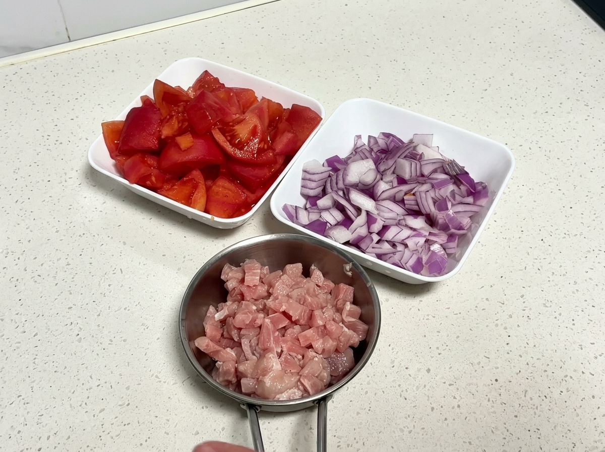 Draufsicht auf drei weiße Schüsseln mit gewürfelten Tomaten, gehackten roten Zwiebeln und gewürfeltem Schweinefleisch.