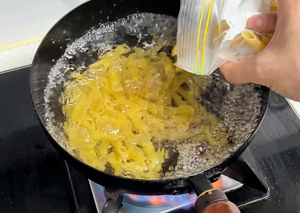 Trockene gelbe Penne werden in einen Topf mit sprudelnd kochendem Wasser geschüttet.