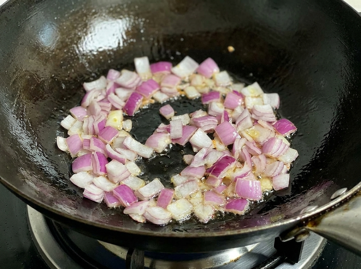 Gehackte rote Zwiebeln braten in einem heißen Wok mit Öl und werden mit einem schwarzen Pfannenwender gerührt.