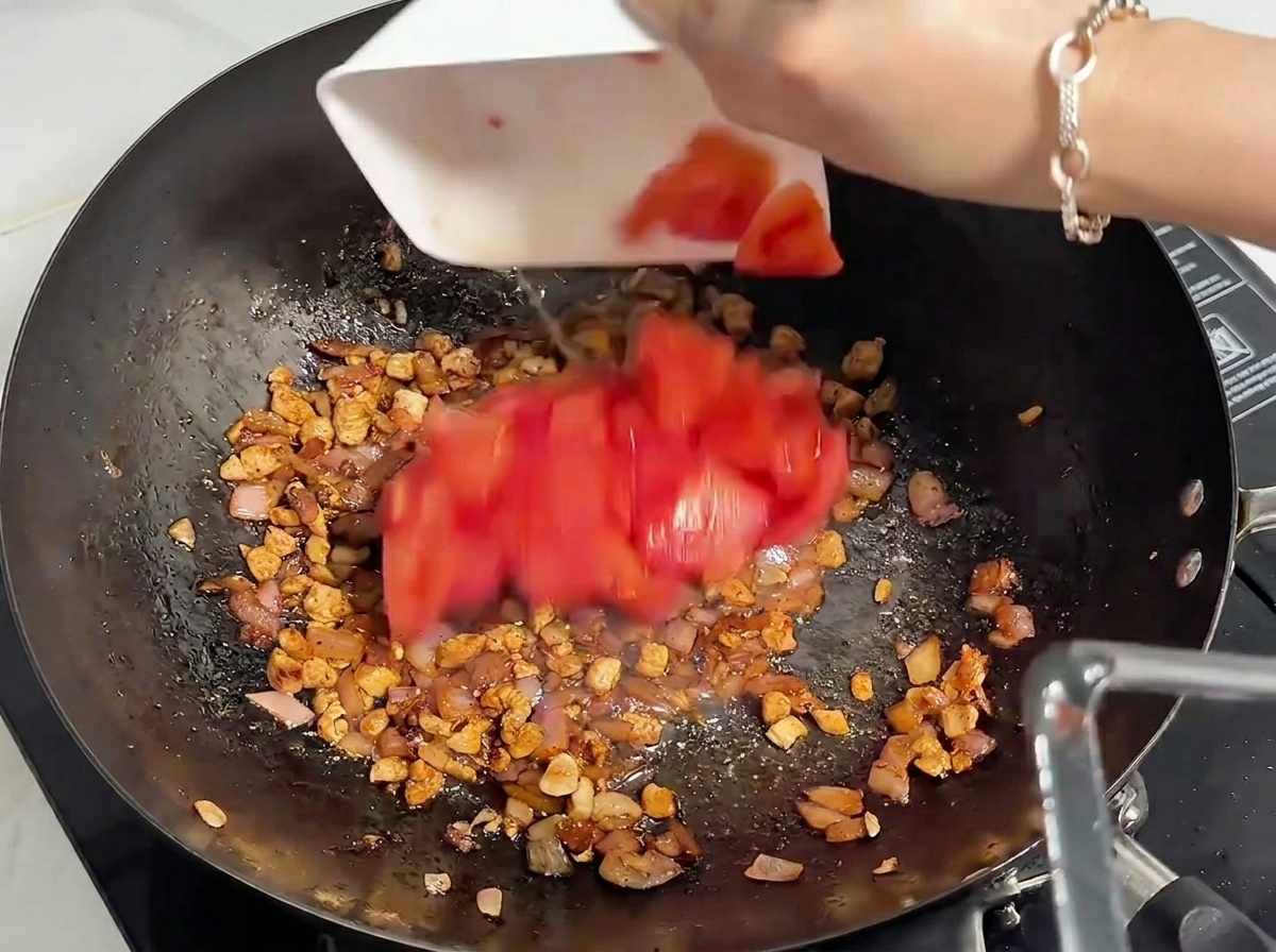 Frisch gehackte rote Tomaten werden aus einer weißen Schüssel in einen Wok mit gegartem Hackfleisch gegeben.