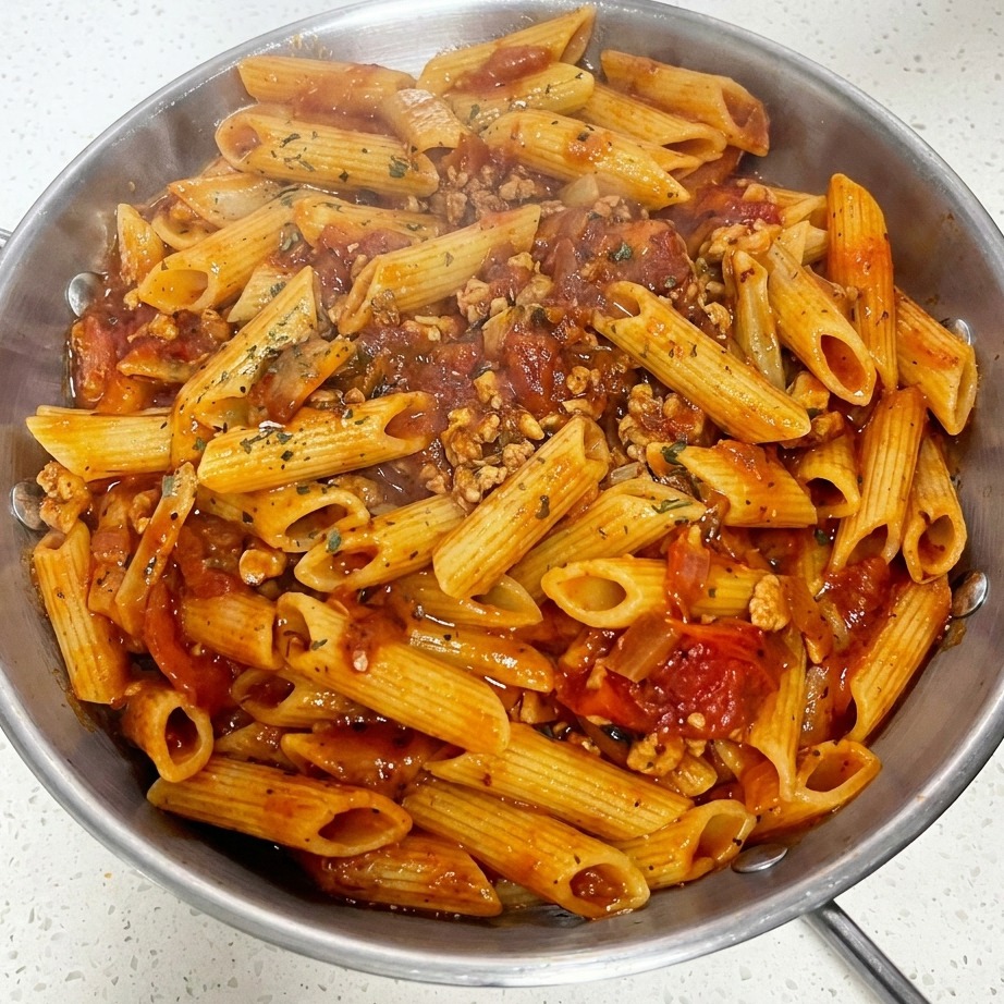 Eine Nahaufnahme einer Pfanne mit Tomaten-Hackfleisch-Makkaroni, garniert mit einer einzelnen Käsescheibe und frisch bestreuten getrockneten grünen Kräutern.