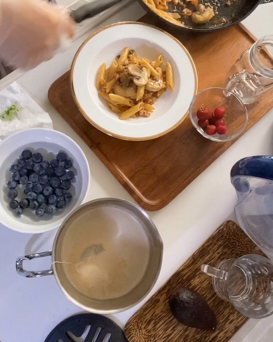 Eine Portion Nudeln mit Fleisch-Pilz-Sauce, angerichtet in einer tiefen weißen Schüssel auf einem Holztablett, daneben frisches Obst.