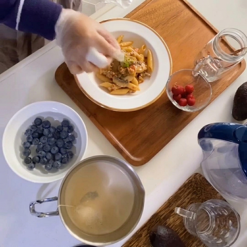 Nahaufnahme einer Hand, die einen Zweig frischen Thymian auf eine Schüssel mit cremigen Pilz-Fleisch-Nudeln legt.