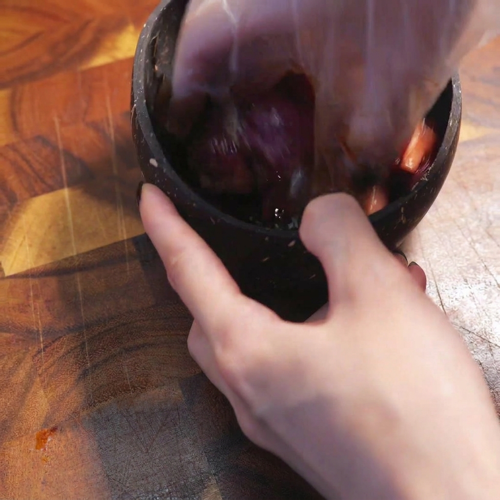 Eine behandschuhte Hand vermischt rohes Rindfleisch mit dunklen Gewürzen in einer Schüssel.