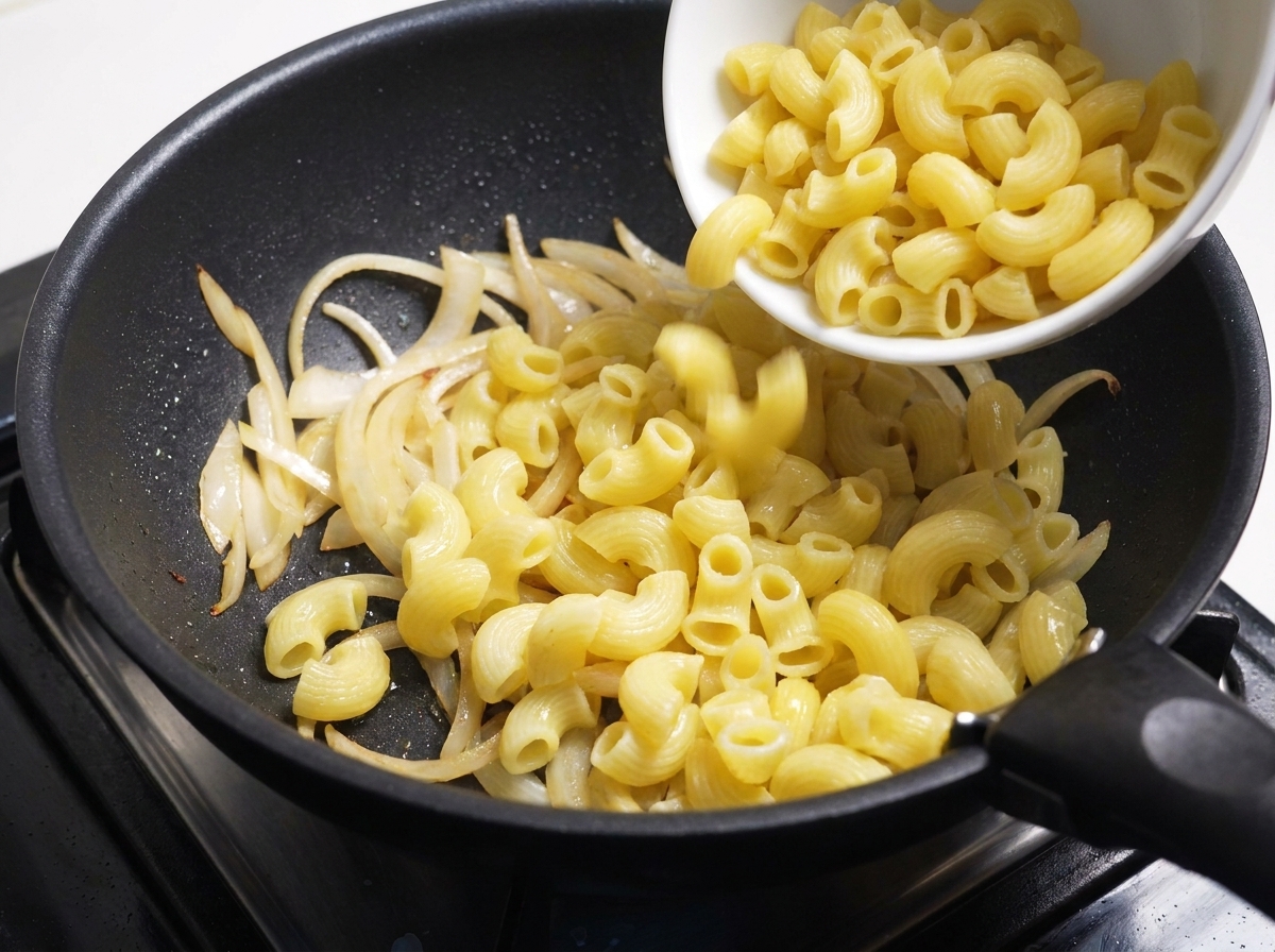 Gekochte Makkaroni werden aus einer weißen Schüssel in die Pfanne mit den Zwiebeln gegeben.
