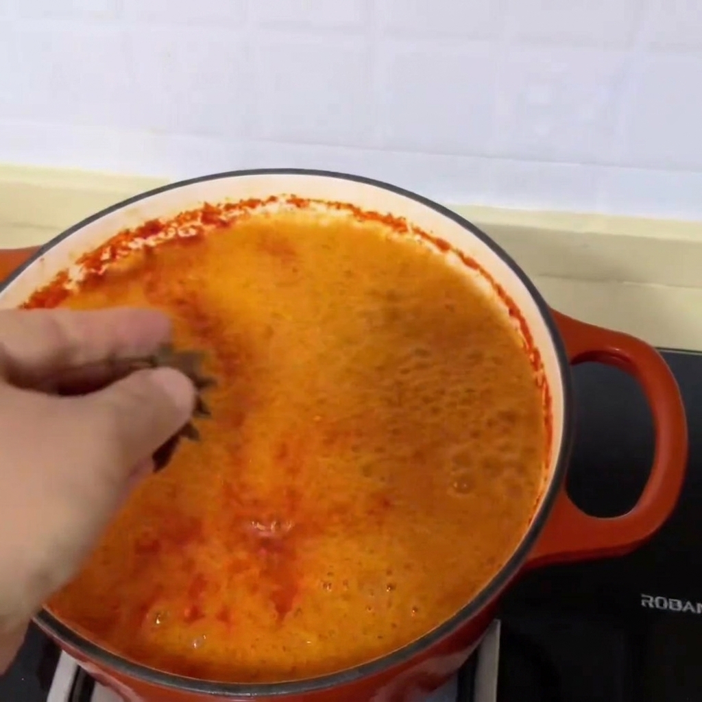 Drei Sternanis-Schoten werden in die leuchtend rote, köchelnde Muschelsuppe gegeben.