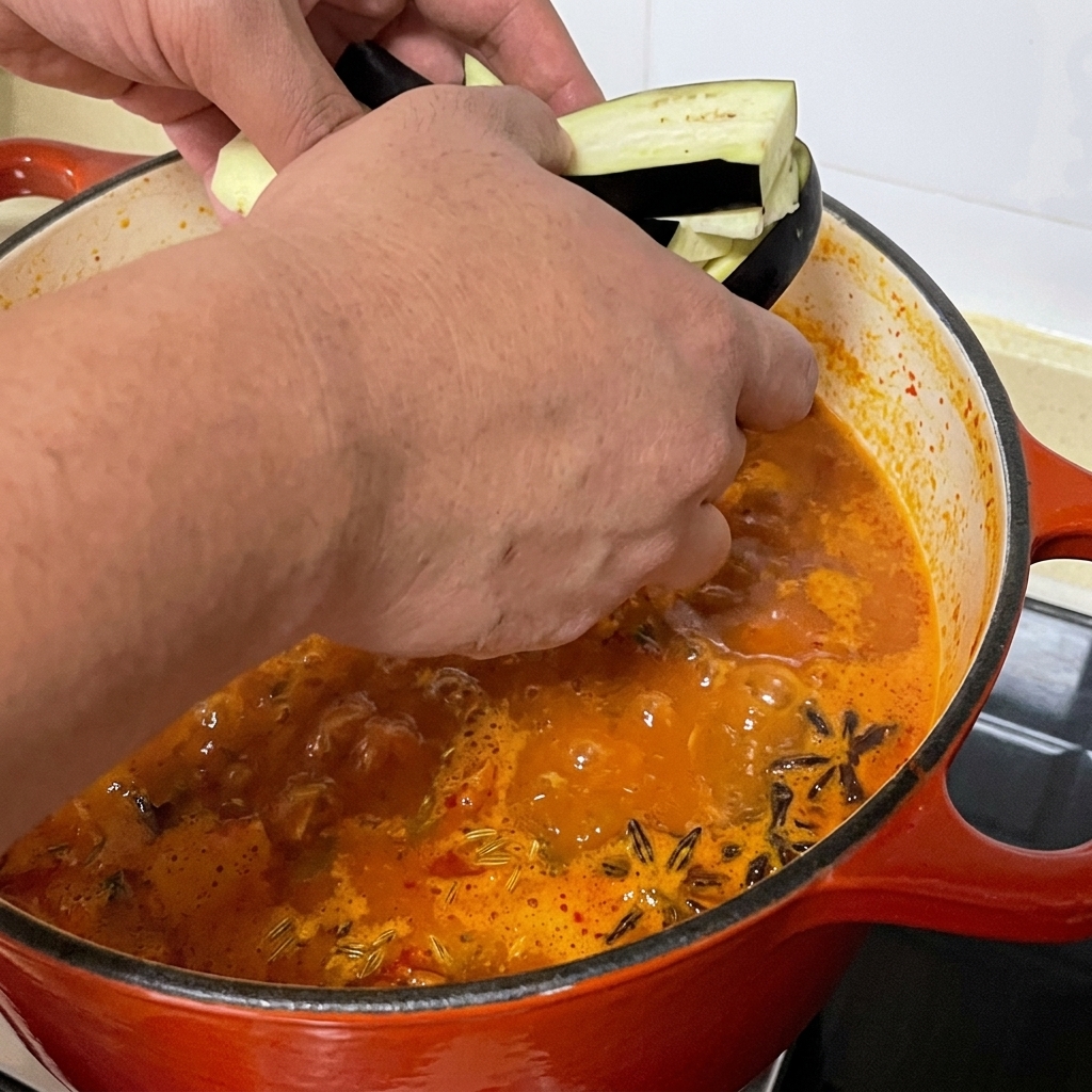 Geschnittene Auberginenstreifen werden in den Topf mit der scharfen Muschelsuppe gegeben.
