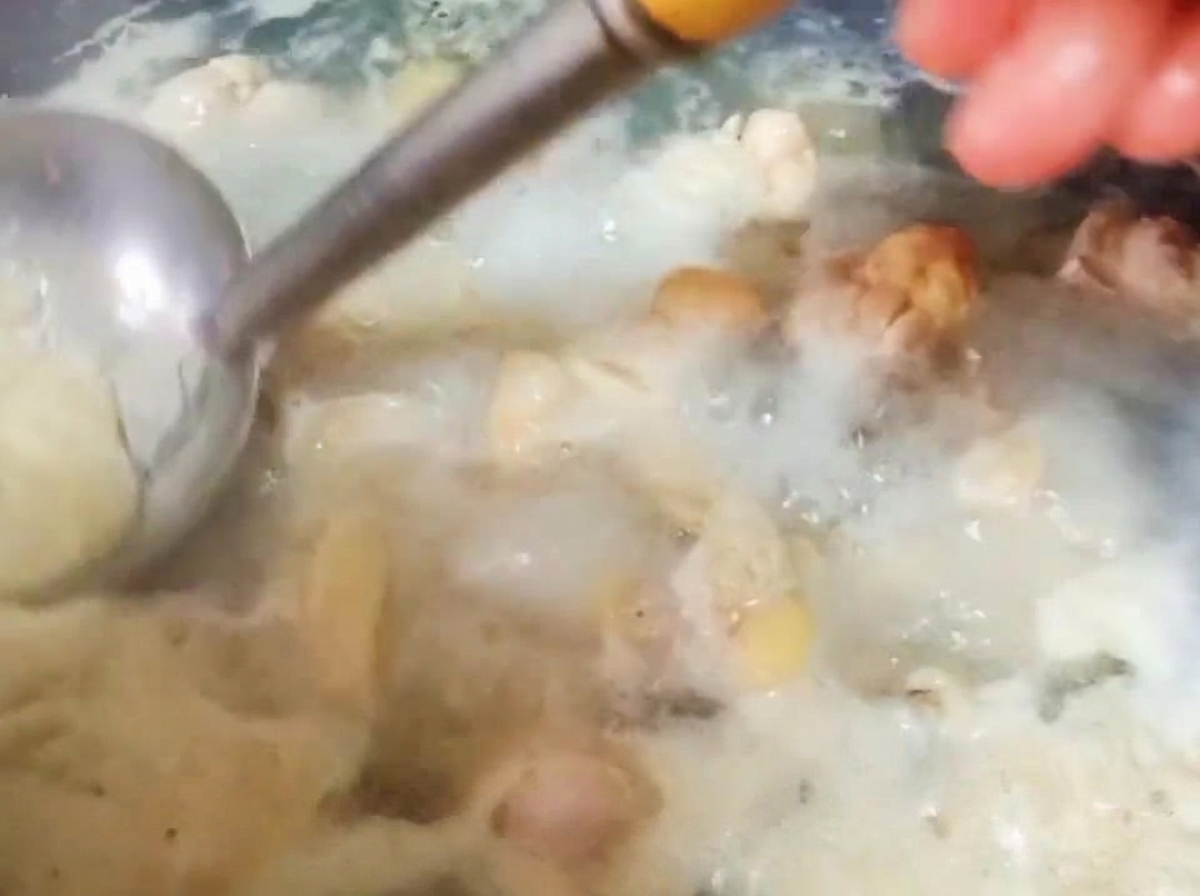 Eine Metallkelle schöpft dicken Blutschaum von der Oberfläche des kochenden Wassers mit den Hähnchenteilen ab.