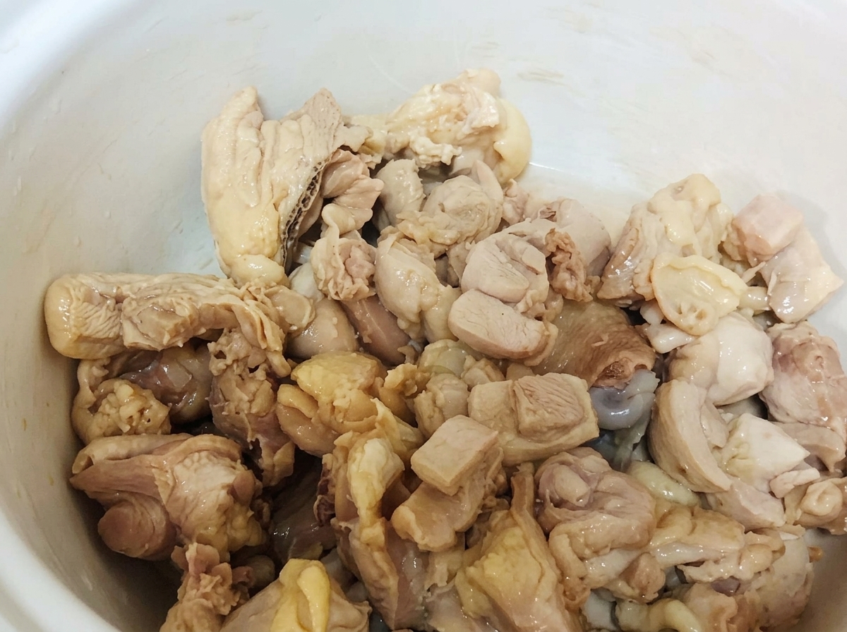 Blanchierte Hähnchenteile ruhen in einem weißen Keramiktopf.