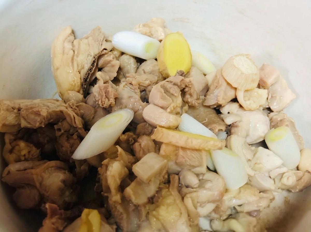 Hähnchenteile in einem Tontopf, gewürzt mit Frühlingszwiebeln, Ingwer und flüssigen Würzmitteln.