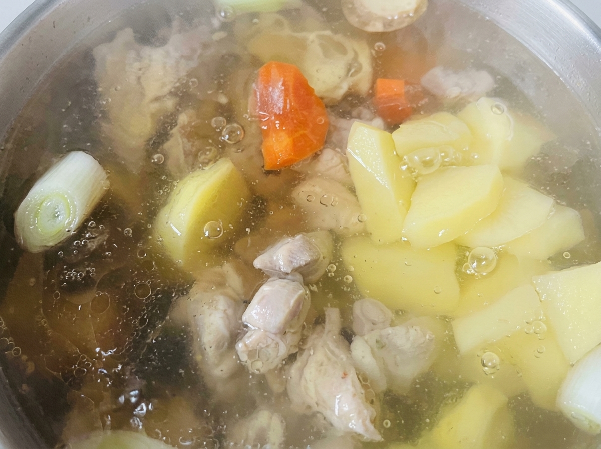 Karotten- und Kartoffelstücke kochen in einer klaren Brühe neben den Hähnchenteilen.