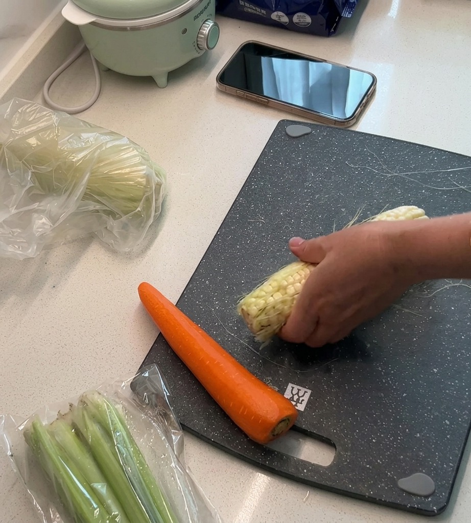 Frische Maiskörner werden auf einem Schneidebrett vom Kolben geschnitten, während die Schale und die Fäden beiseite gelegt werden.