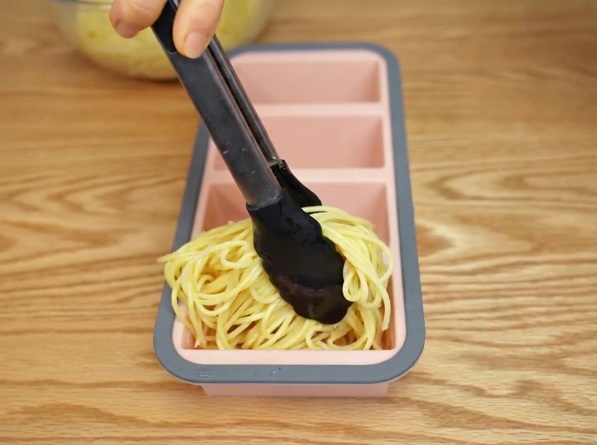 Gekochte Spaghetti werden mit einer Zange in eine Silikonform gefüllt.