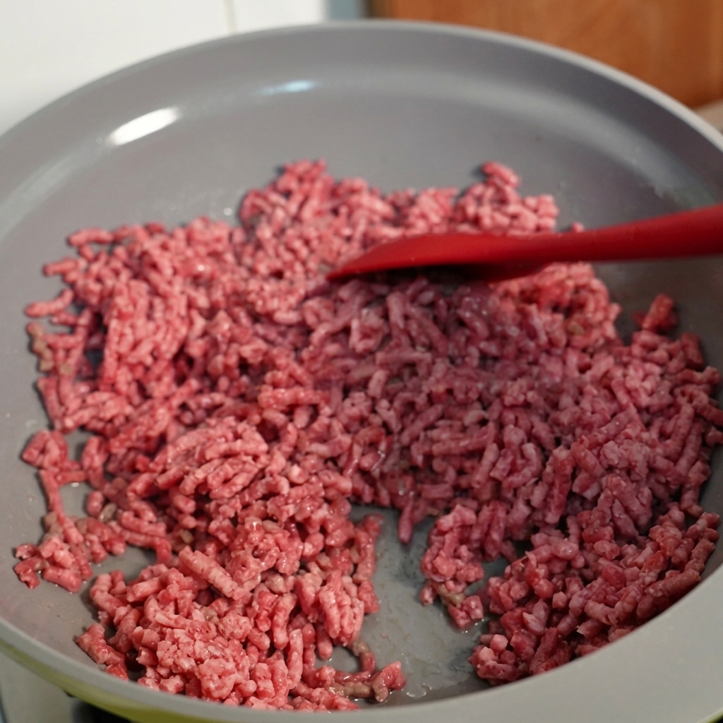 Hackfleisch wird in einer Pfanne gerührt und zeigt eine gebräunte Textur.