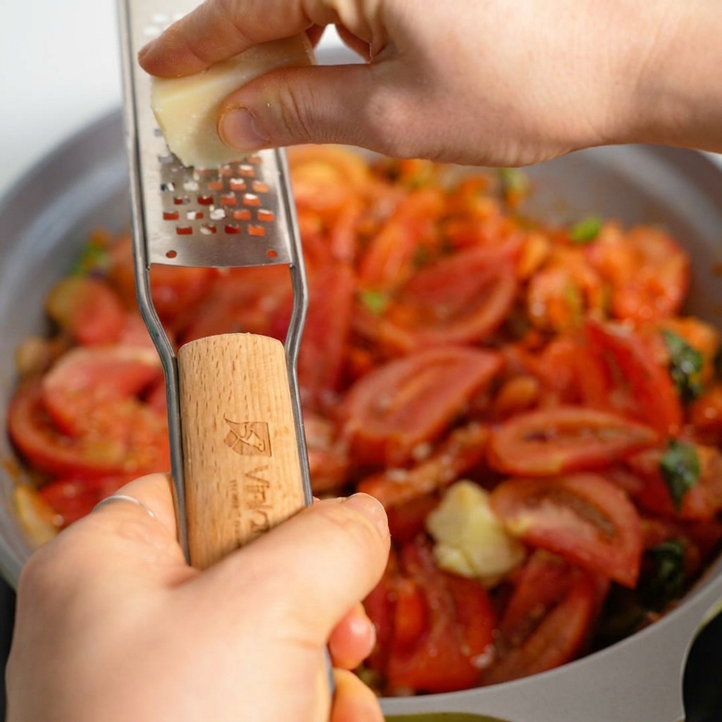 Frischer Parmesan wird direkt in eine Pfanne mit blubbernder, herzhafter Tomaten-Hackfleisch-Sauce gerieben.