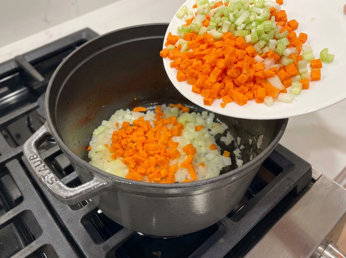 Gewürfelte Karotten und Sellerie werden in den Topf zu den Zwiebeln geschüttet.