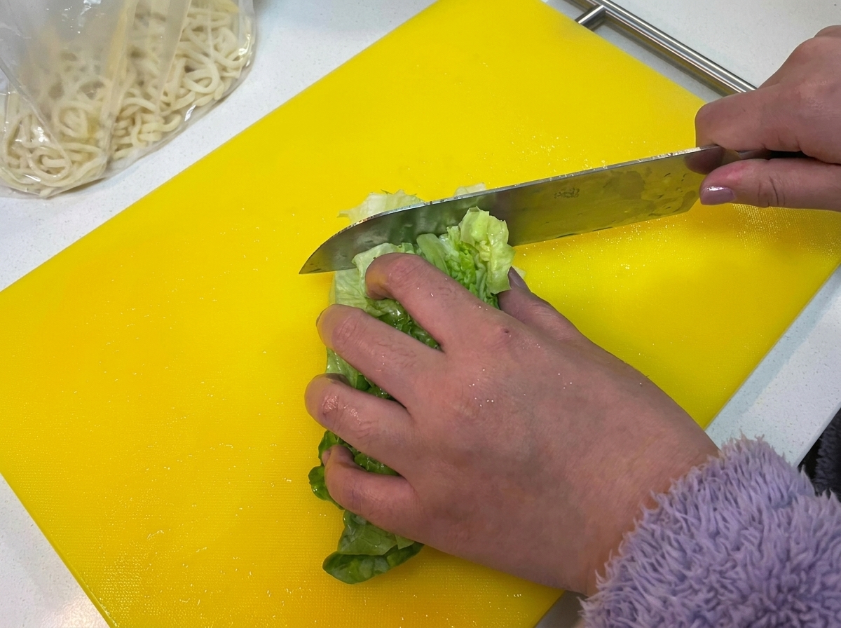 Frische grüne Salatblätter werden auf einem leuchtend gelben Schneidebrett gehackt.