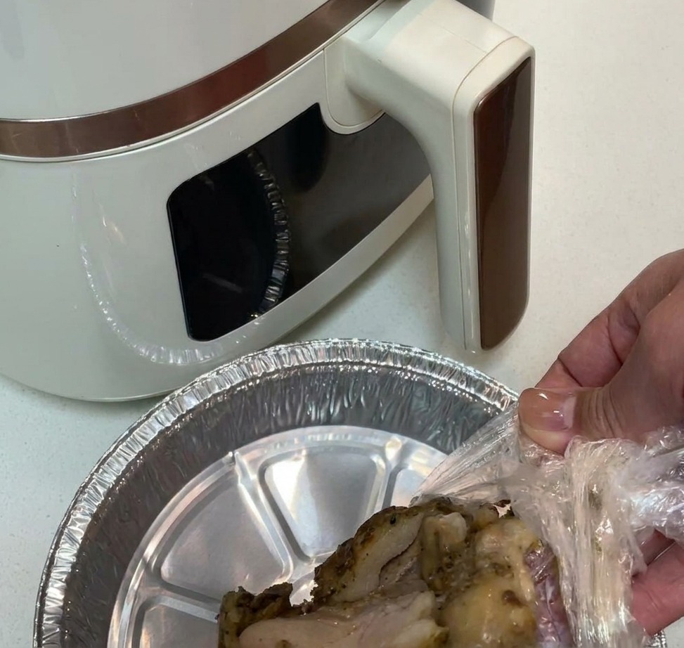 Vorgewürztes Hähnchenschenkelfleisch wird in einen mit Aluminiumfolie ausgekleideten Korb der Heißluftfritteuse gelegt.