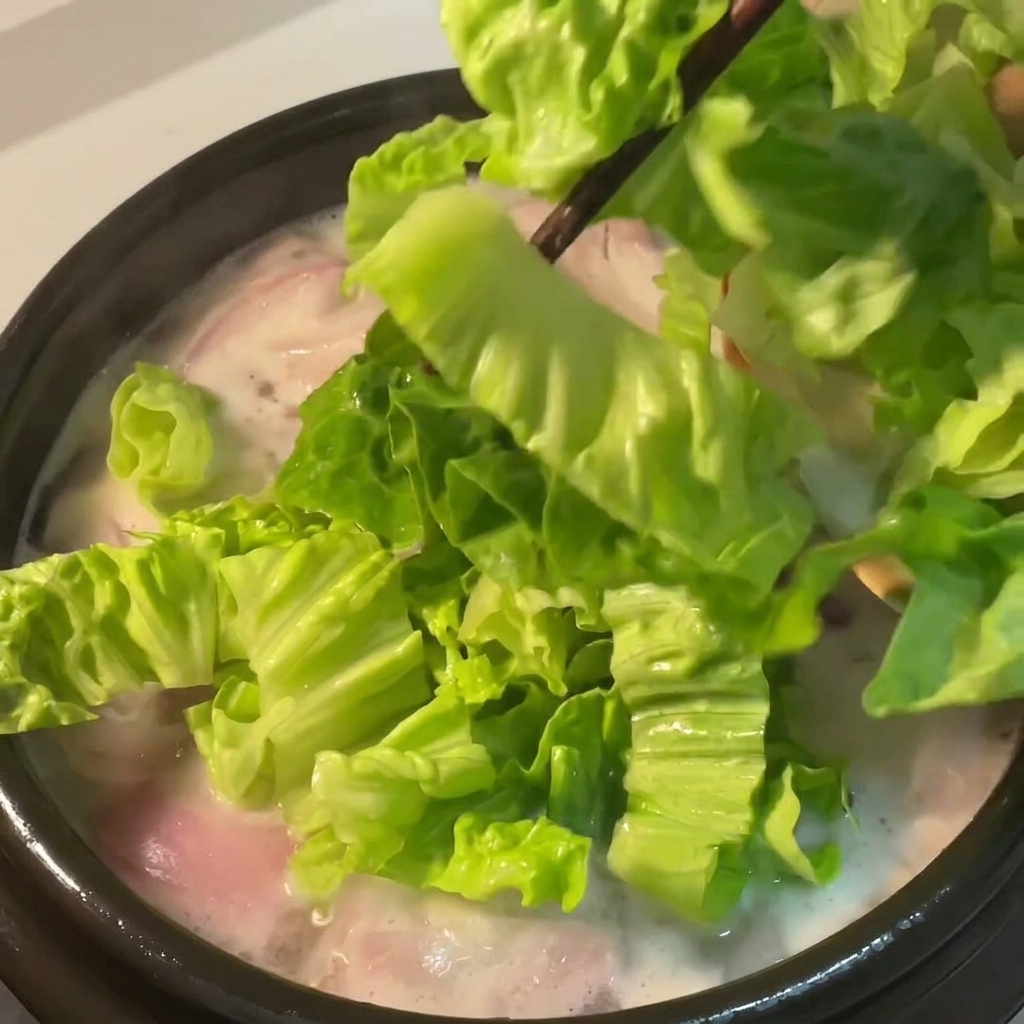 Frischer grüner Salat wird in die köchelnde Hühnersuppe mit roten Zwiebeln gegeben.