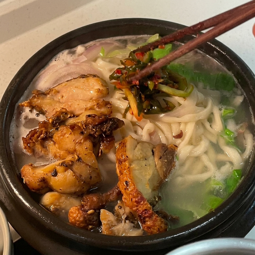 Leuchtend rotes Frühlingszwiebel-Kimchi wird als Garnitur auf die Hühnernudelsuppe gegeben.