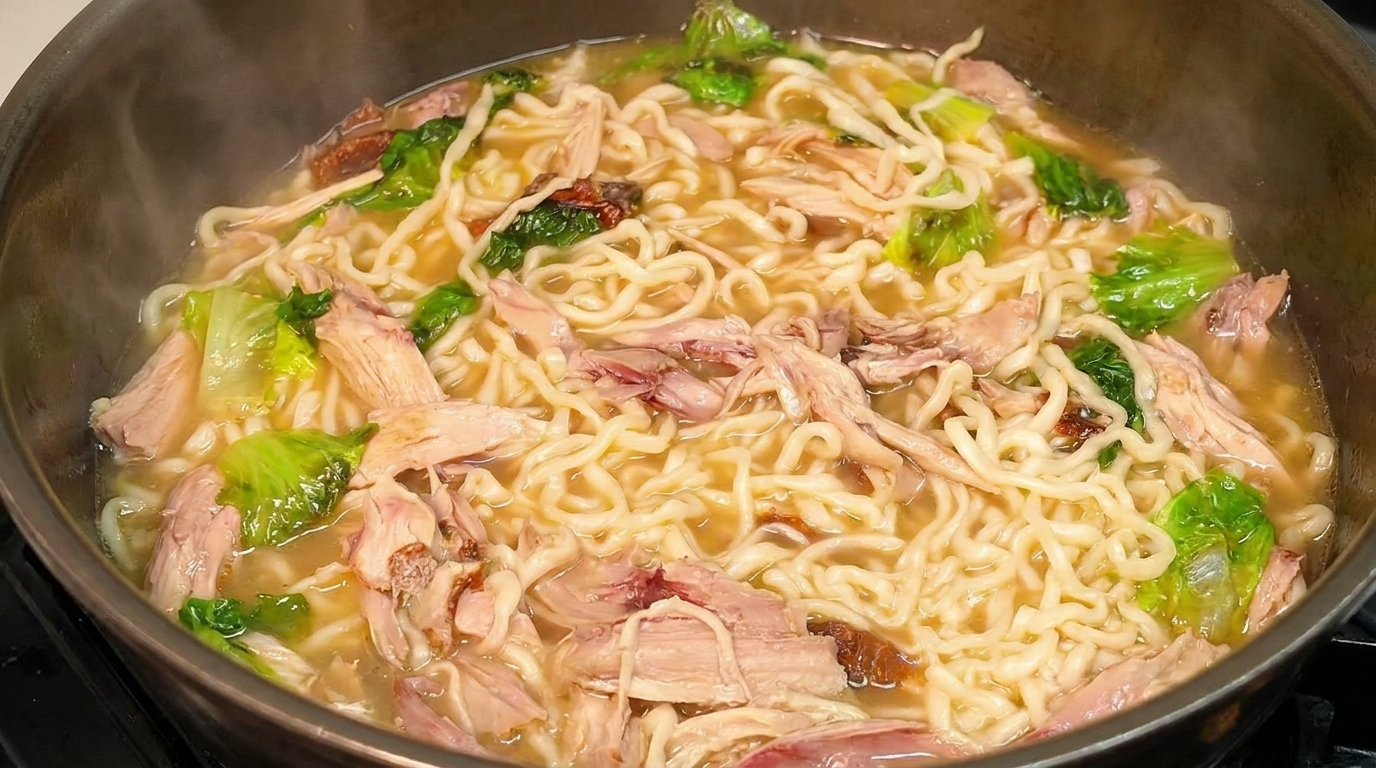 Ein dampfender Topf Hähnchen-Nudelsuppe mit Wellennudeln, zerkleinertem Pfeffer-Hähnchen und frischem Salat.