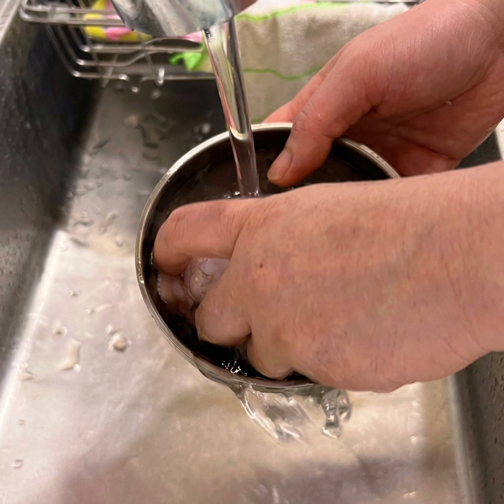 Frische Hühnerflügel werden in einer Metallschüssel unter fließendem Wasser gewaschen.