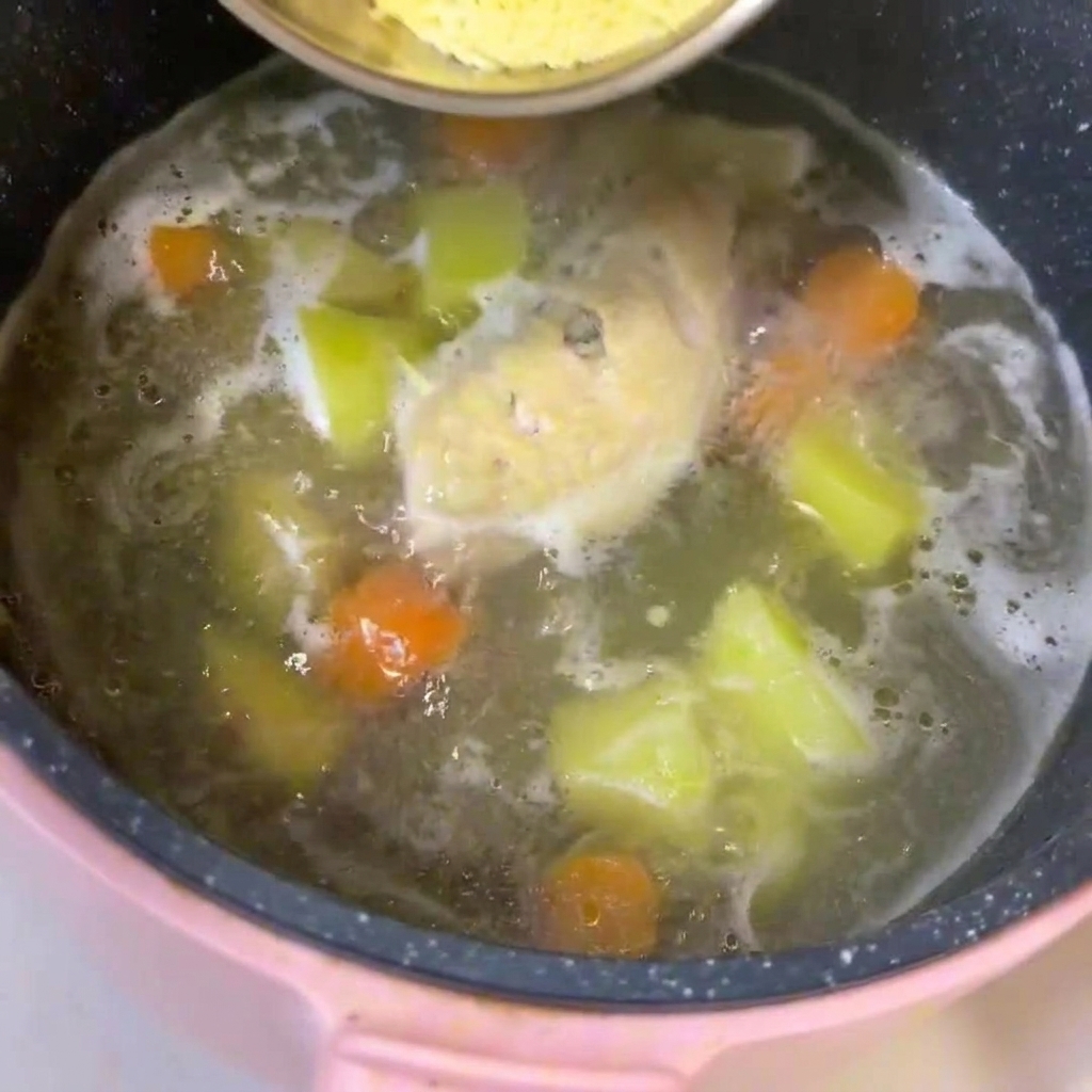 Ein Topf mit köchelnder Hühnerbrühe, Fleisch, Kartoffeln und Karotten, in den Babynudeln gerührt werden.