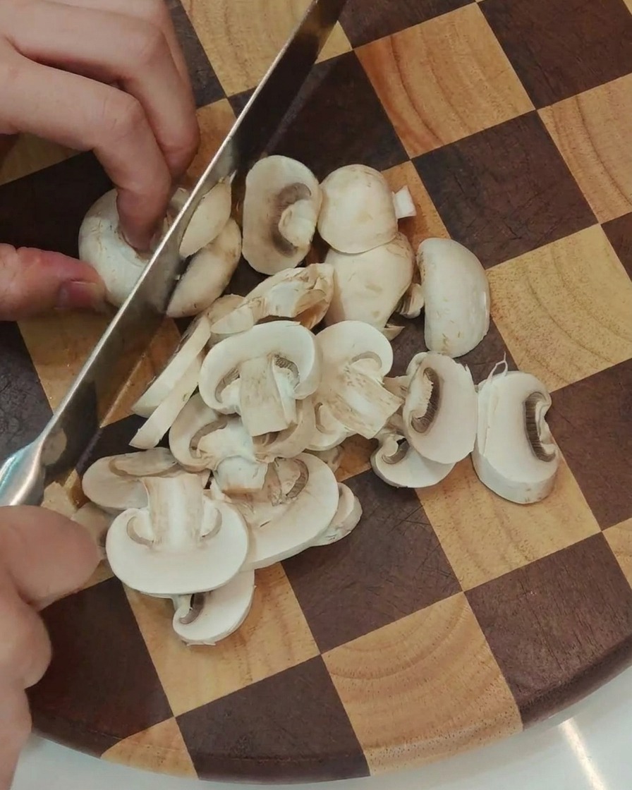 Frische weiße Champignons werden in gleichmäßige Scheiben geschnitten.