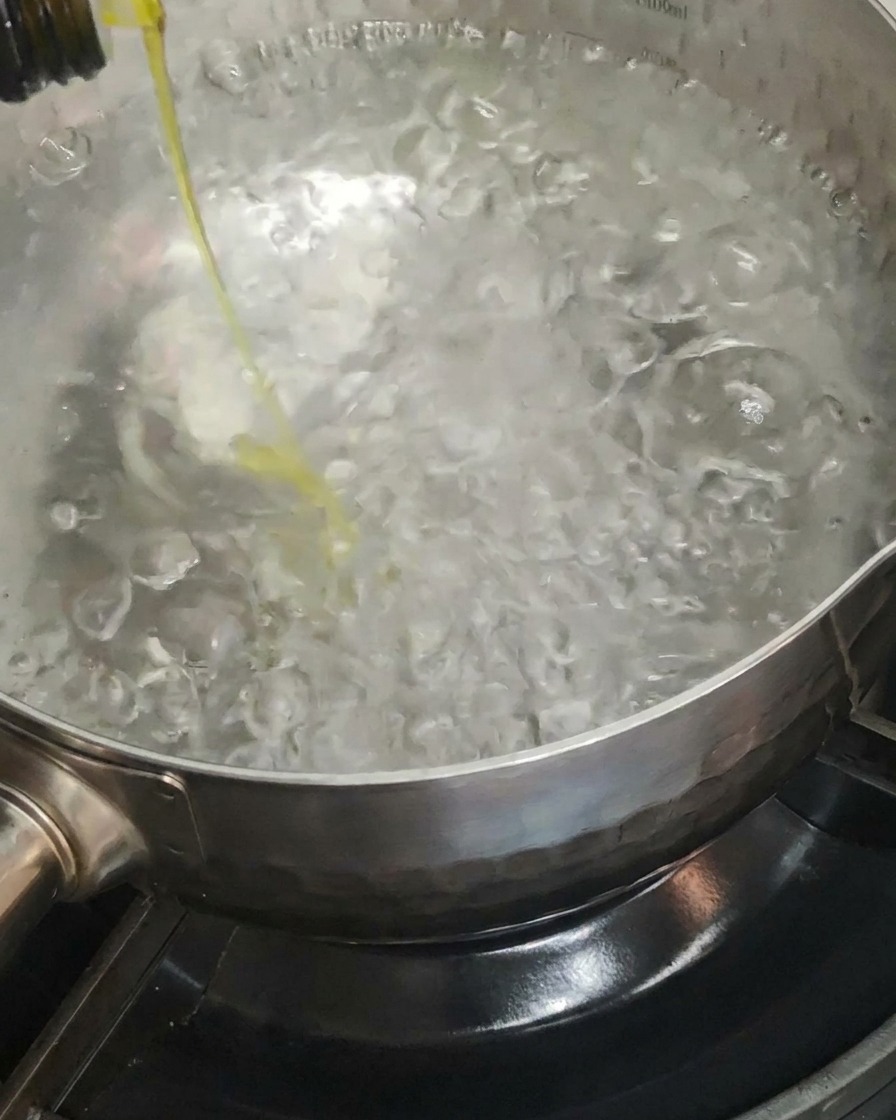 Olivenöl wird in einen großen Topf mit kochendem Wasser gegeben.
