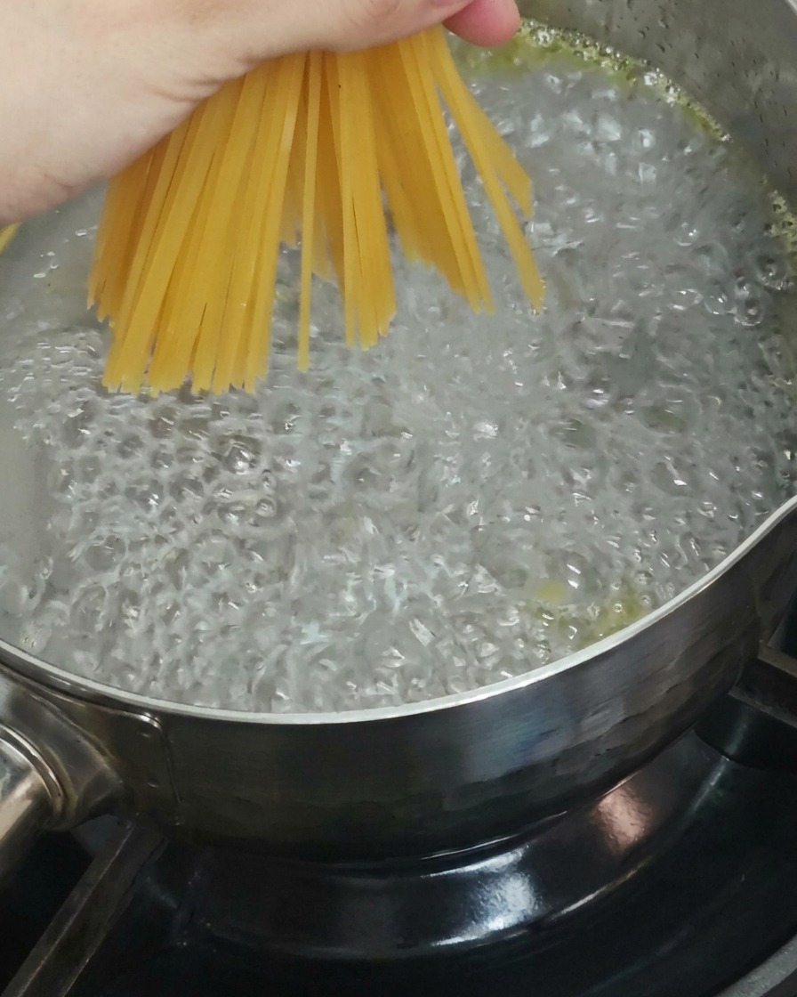Nahaufnahme einer Hand, die Spaghetti in kochendes Wasser gibt.