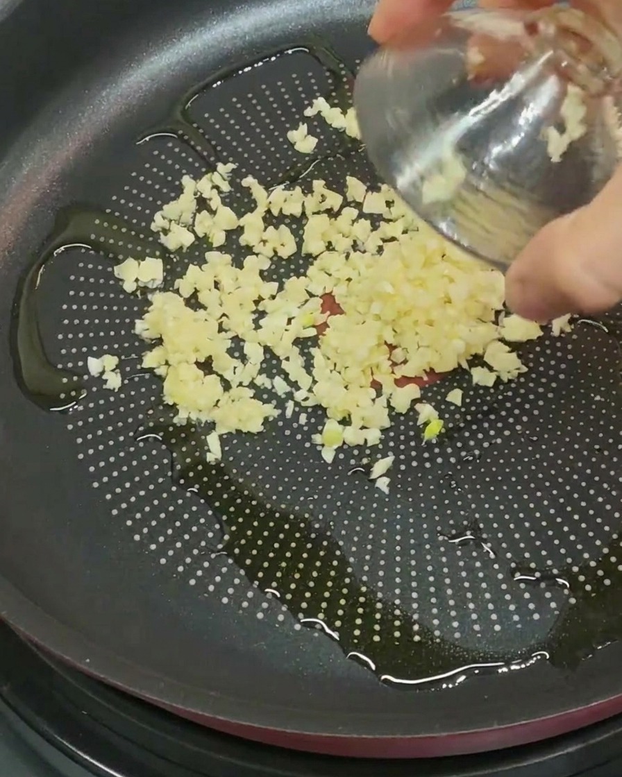 Fein gehackter Knoblauch wird in eine Pfanne mit Öl gegeben.