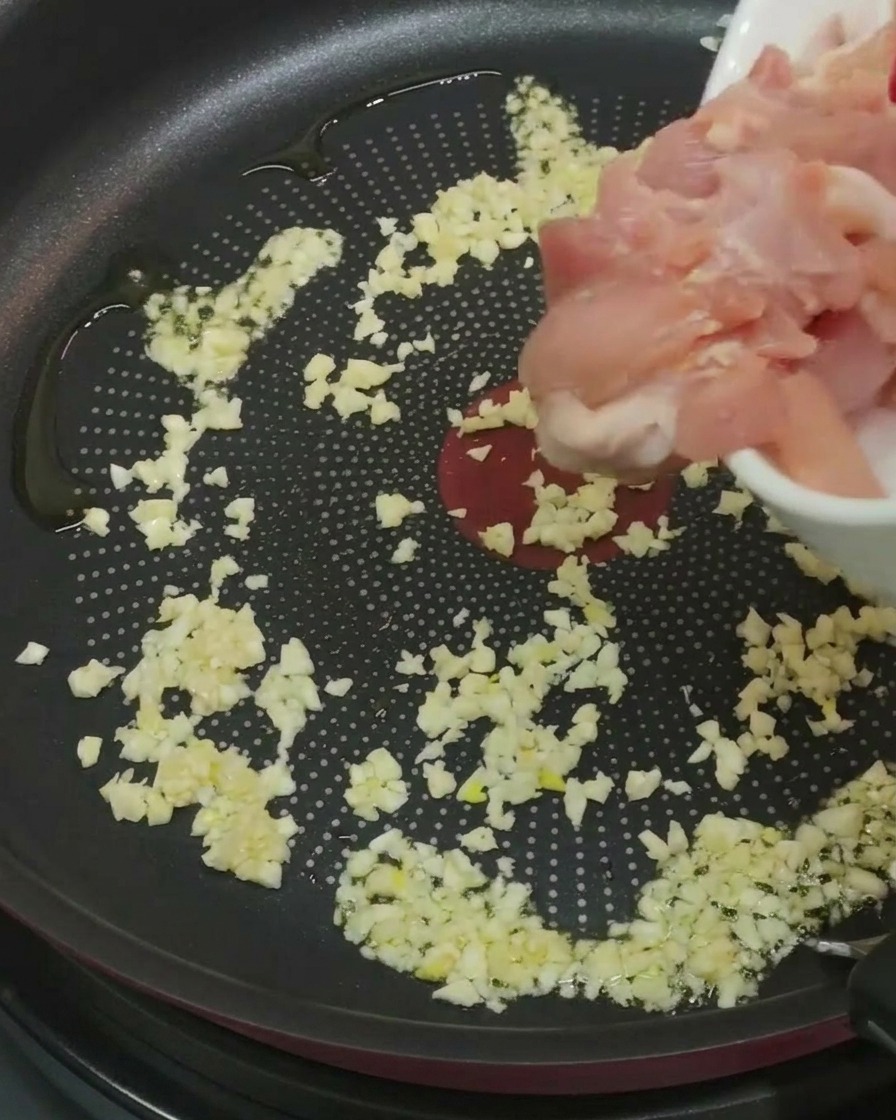 Hähnchenstücke werden in die Pfanne zu Knoblauch und Öl gegeben.