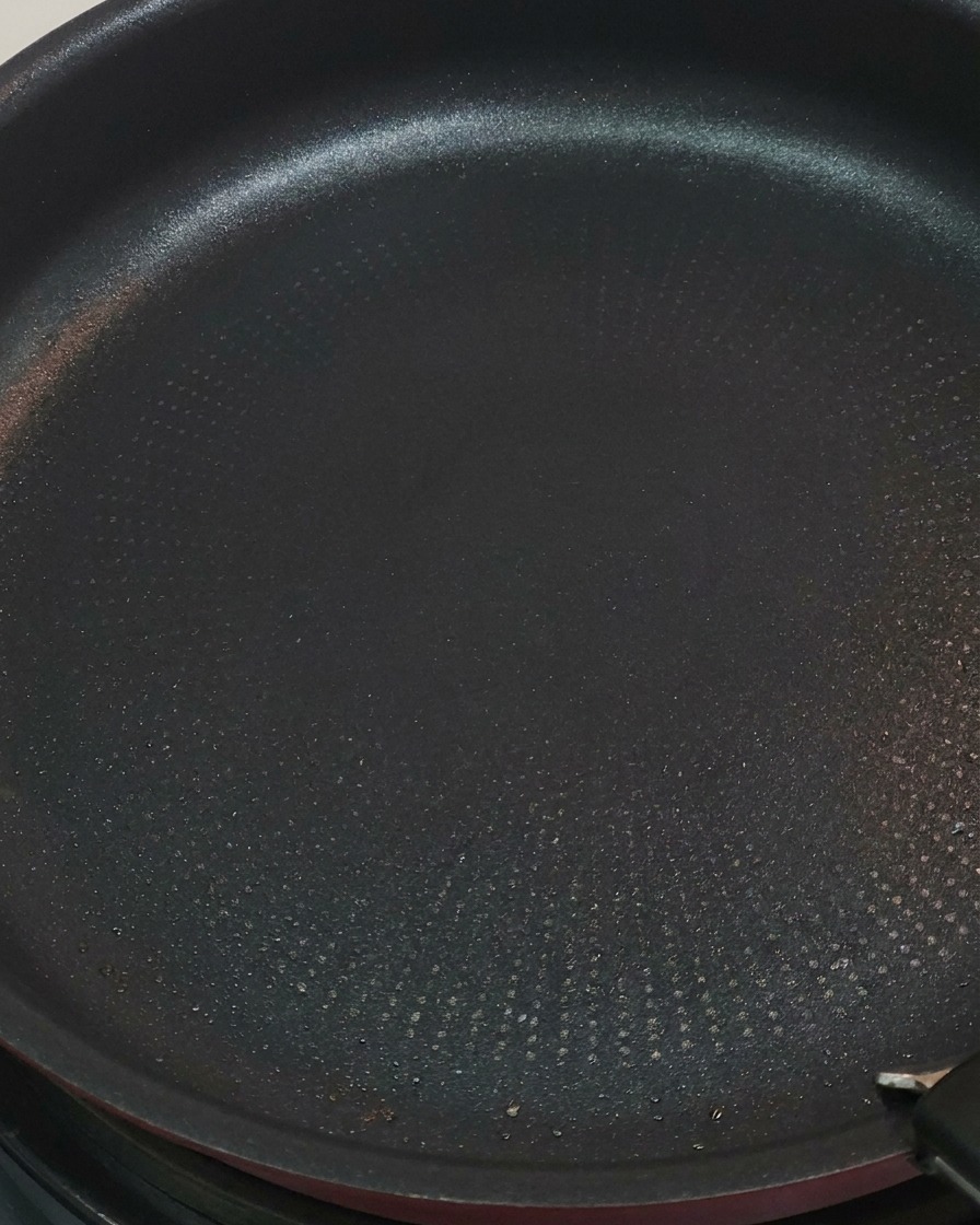 Hähnchenstücke in einer Pfanne werden mit einer Zange gewendet.