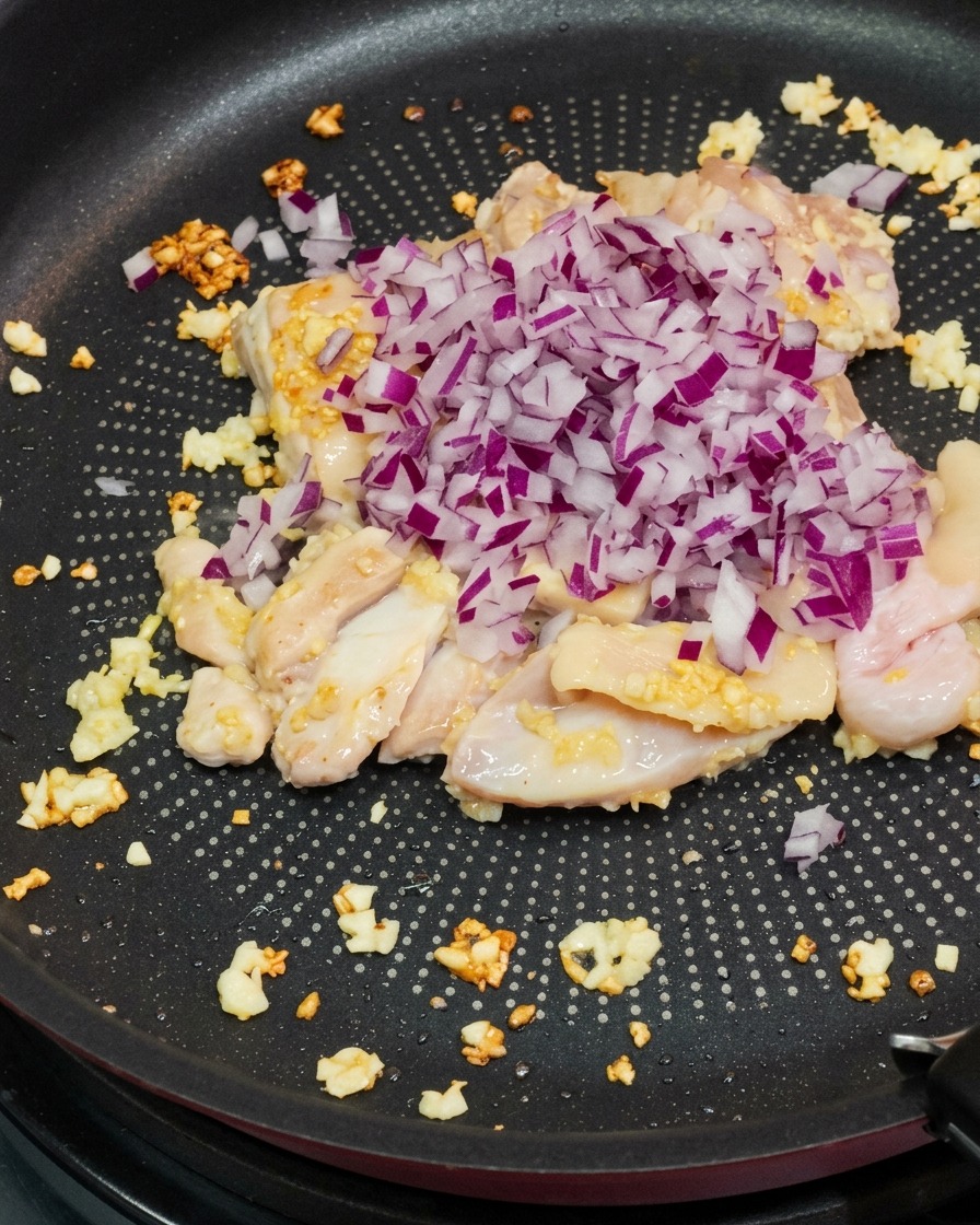 Gewürfelte rote Zwiebeln kommen zum angebratenen Hähnchen.