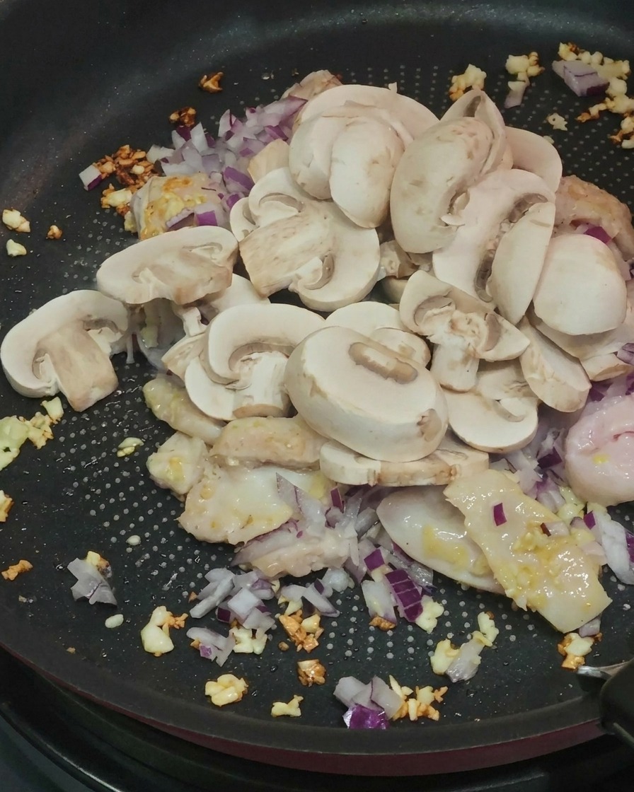 Geschnittene Champignons werden zum Hähnchen in die Pfanne gegeben.