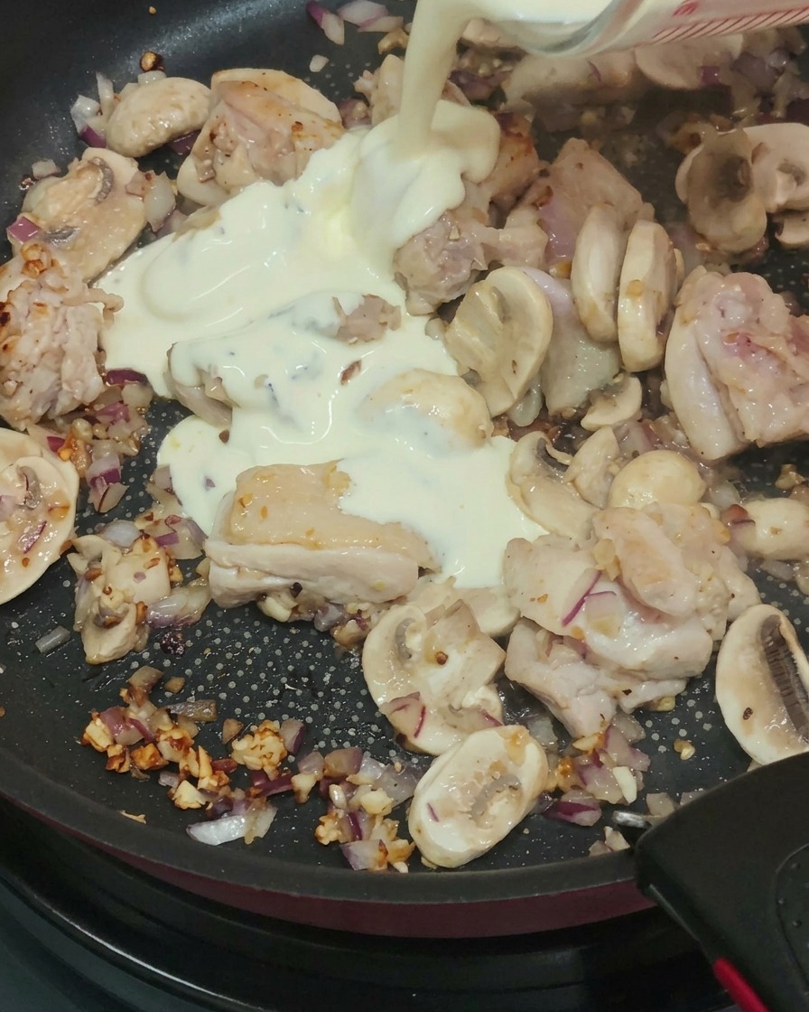 Sahne wird in die Pfanne mit Hähnchen und Pilzen gegossen.