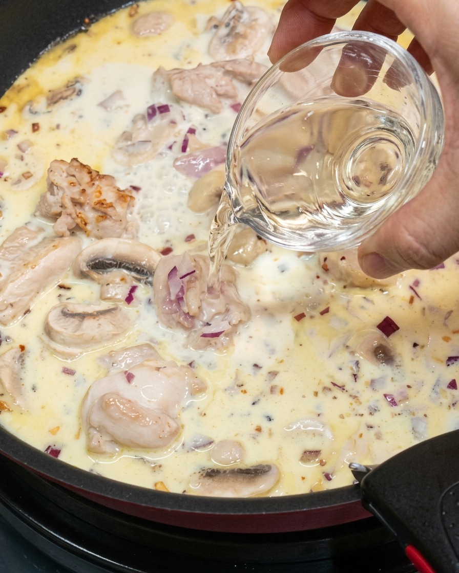 Ein Schuss Weißwein wird in die köchelnde Sauce gegossen.