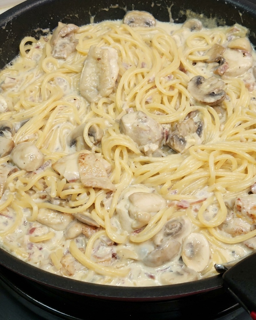 Spaghetti werden in der cremigen Sauce gewendet.
