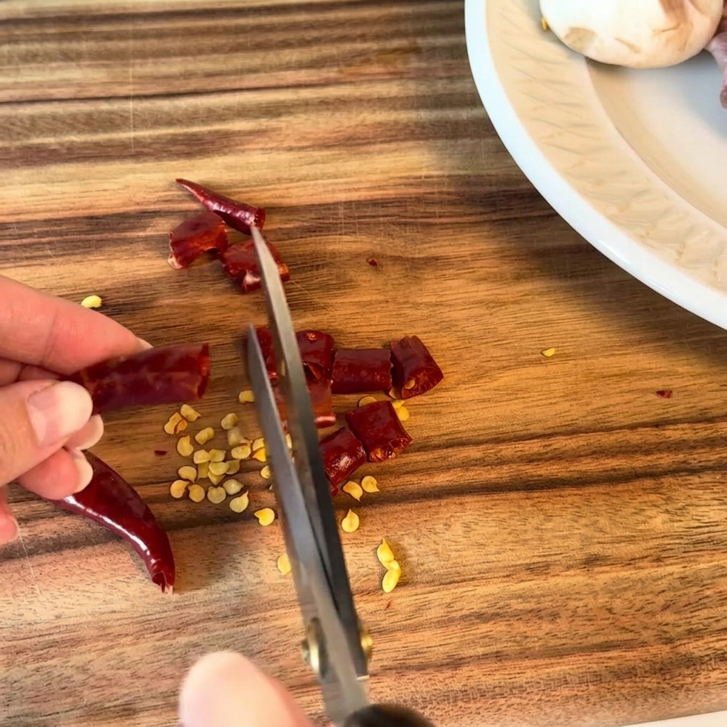 Getrocknete Chilischoten werden mit einer Küchenschere in kleine Stücke geschnitten.