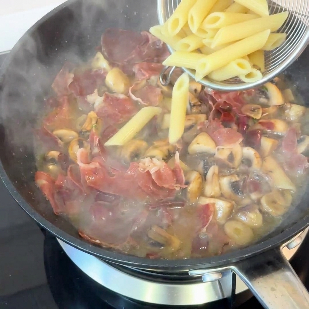 Gekochte Penne werden mit einem Seiher in die Pfanne zur Sauce gegeben.